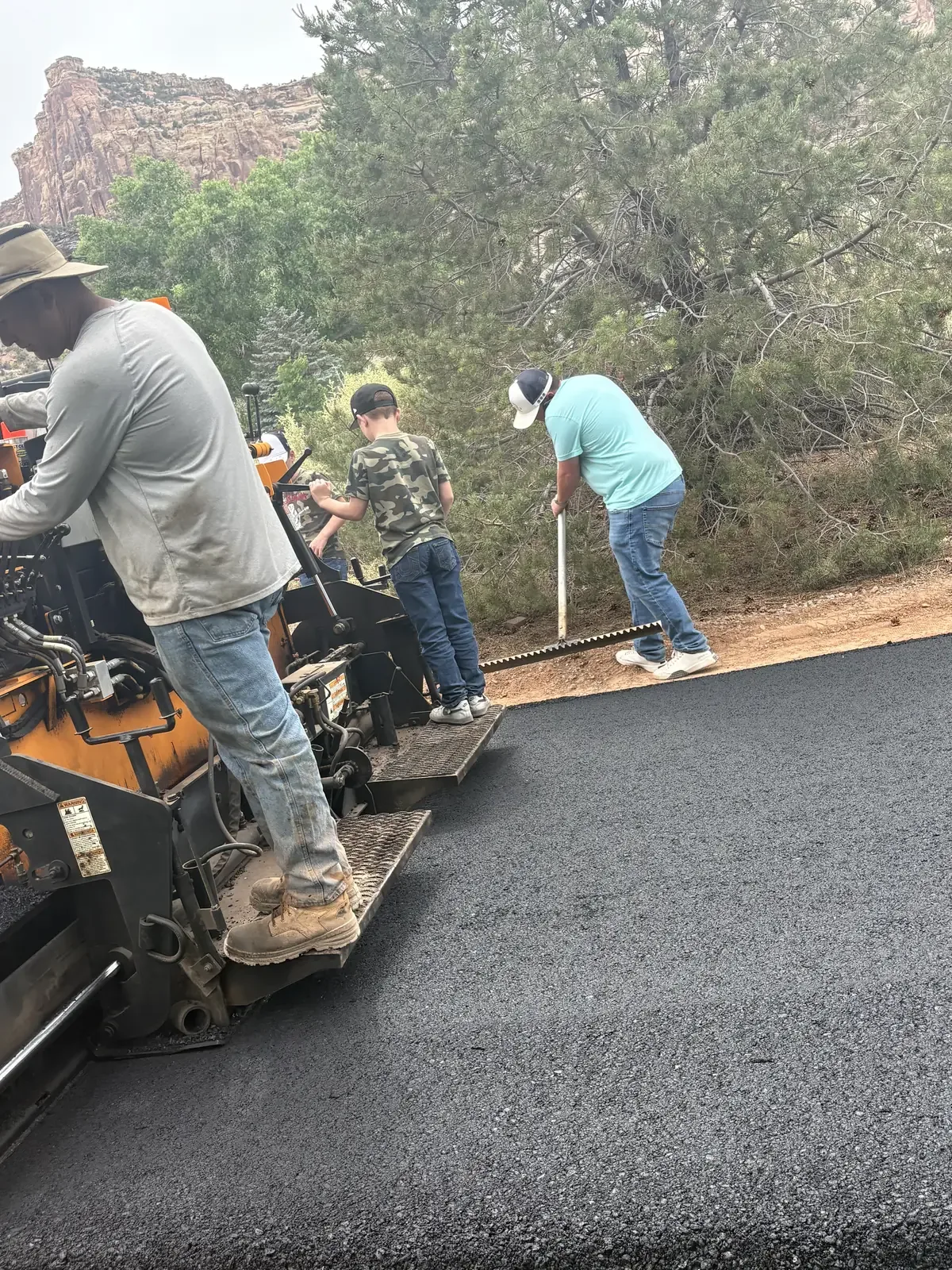 Crew hand working hot asphalt behind the paver