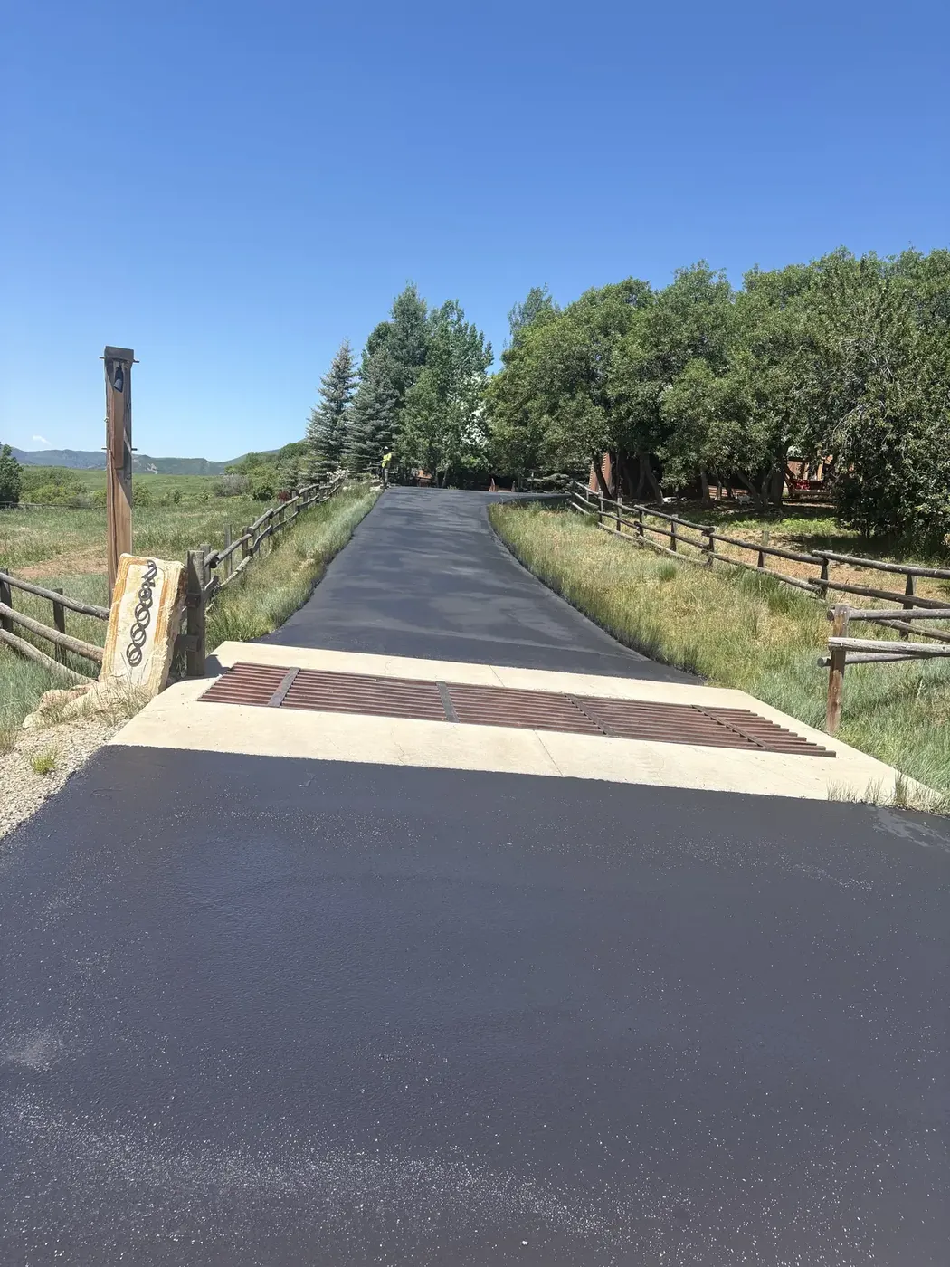 Straight new asphalt lane between rail fences at a ranch