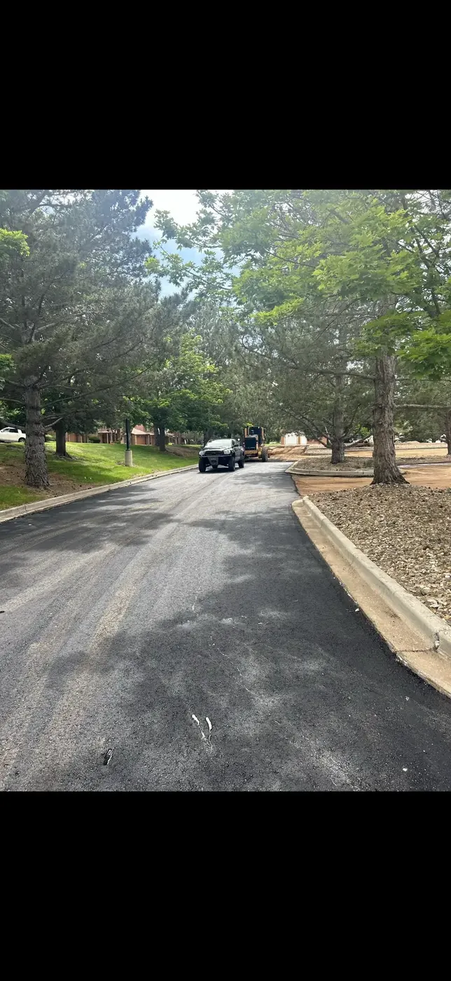 Freshly paved driveway through pine trees with a work truck parked