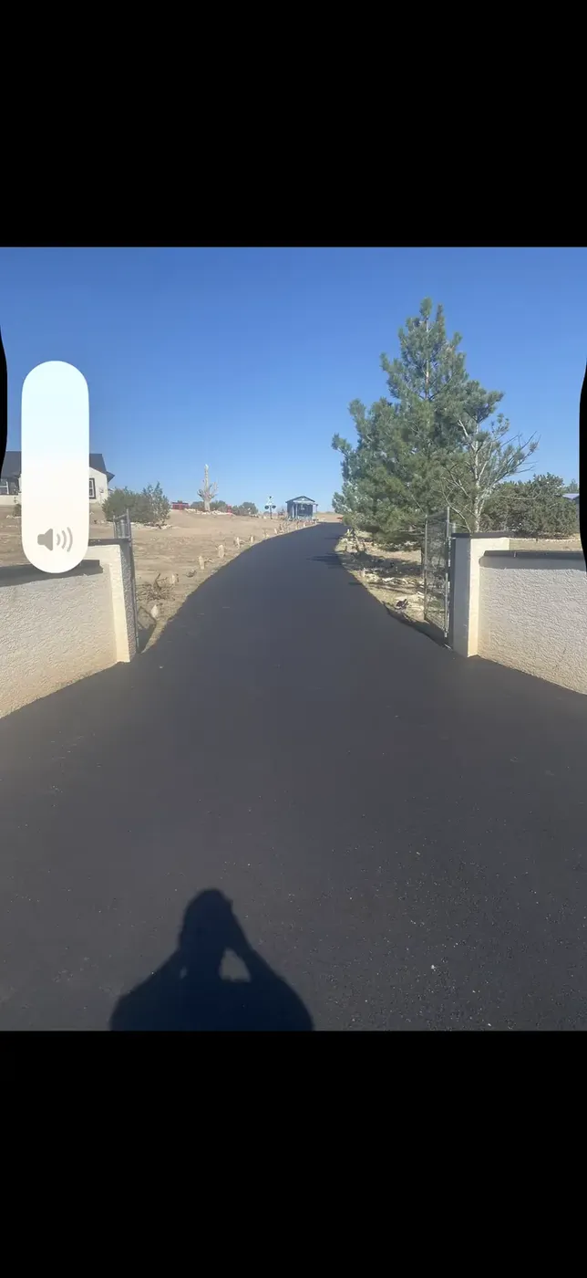 Dark new asphalt drive passing between stucco entry walls