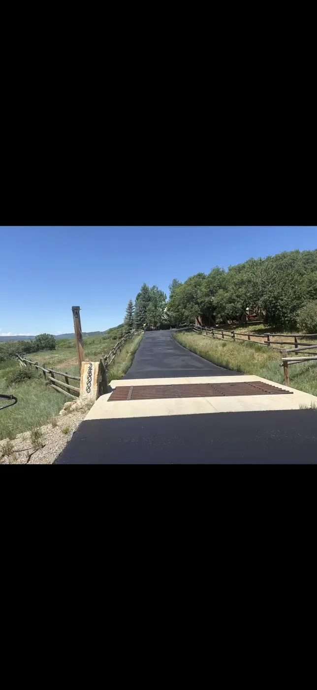 Asphalt drive meeting a new concrete apron at a rail fence
