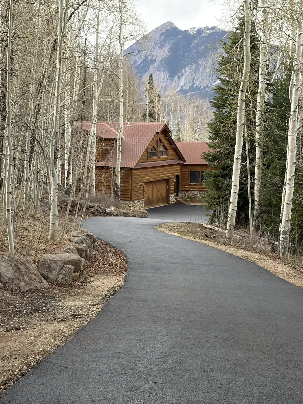 Curved asphalt driveway through aspen trees to a cabin — near Larkspur, CO