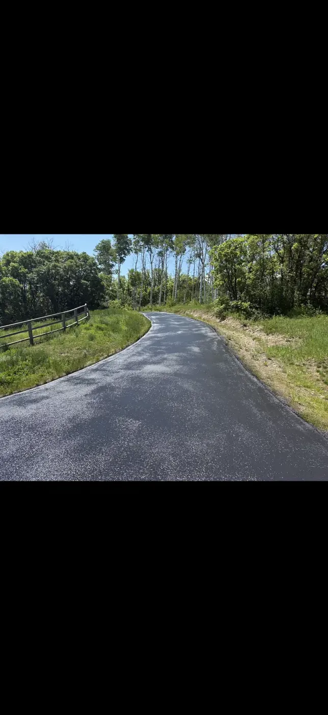 New asphalt drive curving along a wood rail fence past pasture