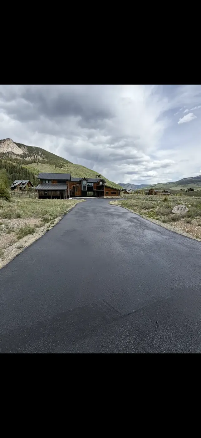 Wide new asphalt approach to a mountain home under gray skies
