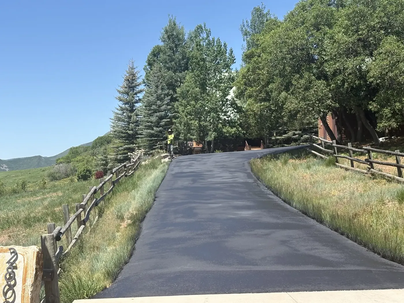 Crew finishing the edges of a new asphalt drive near the pines
