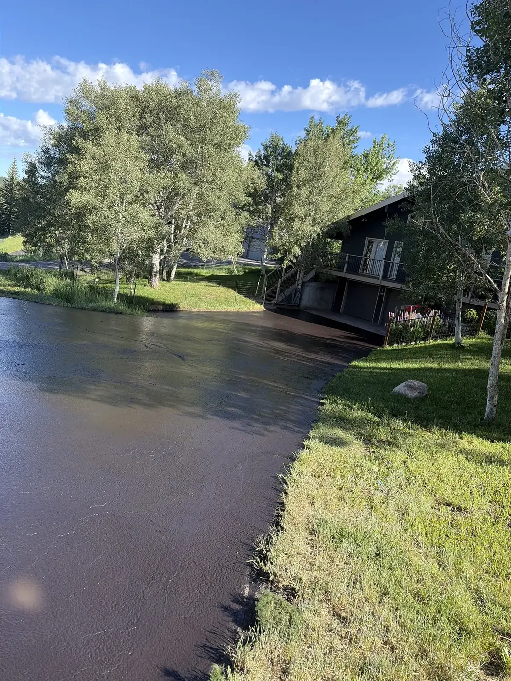 Freshly sealed driveway beside a pond and a lake house